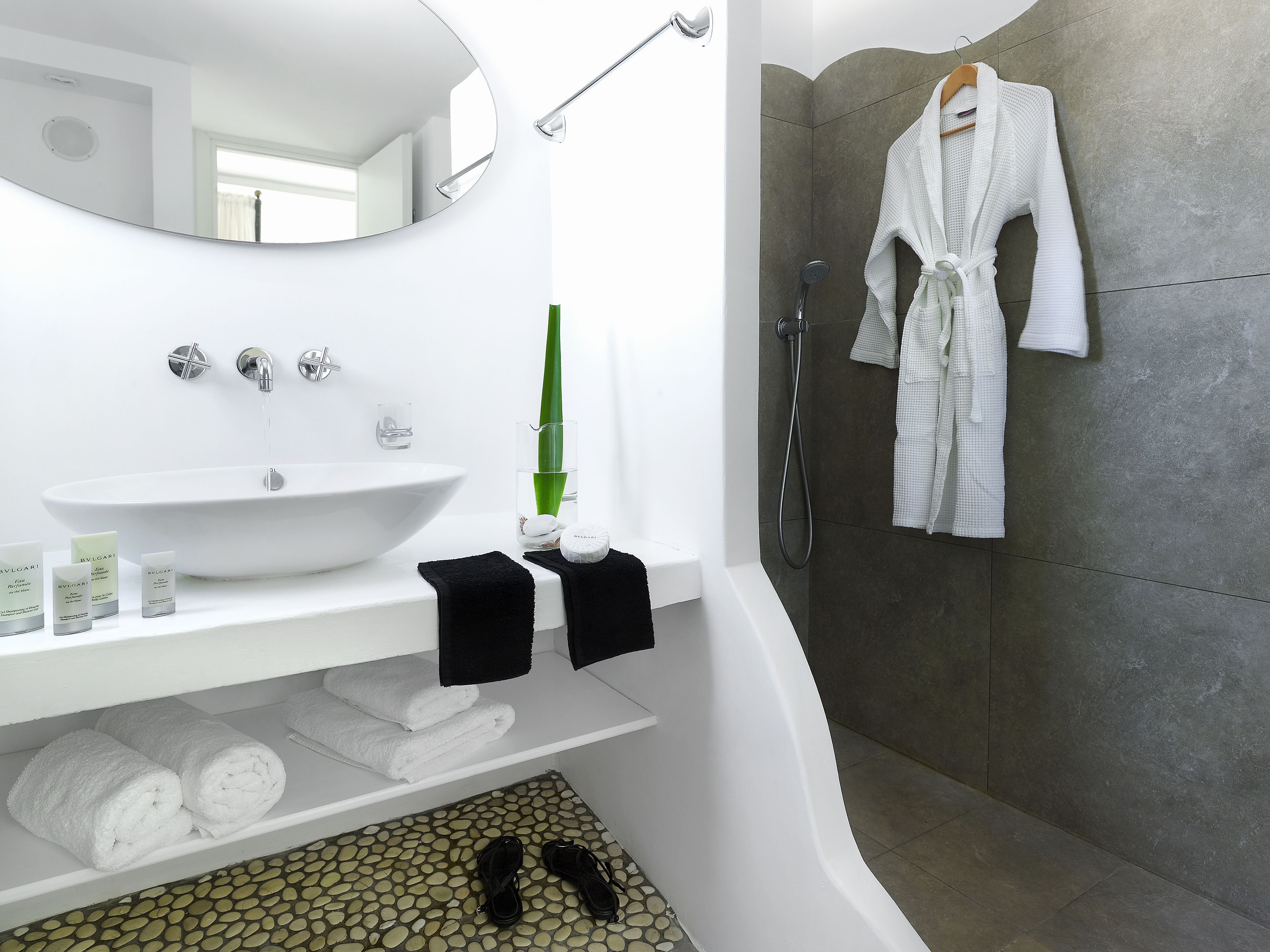 A modern bathroom with a white sink, mirror, and shower. There are towels and toiletries on the counter.