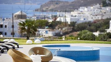 Zona de piscina con sillas de descanso y una pequeña piscina, rodeada de follaje y edificios blancos al fondo.