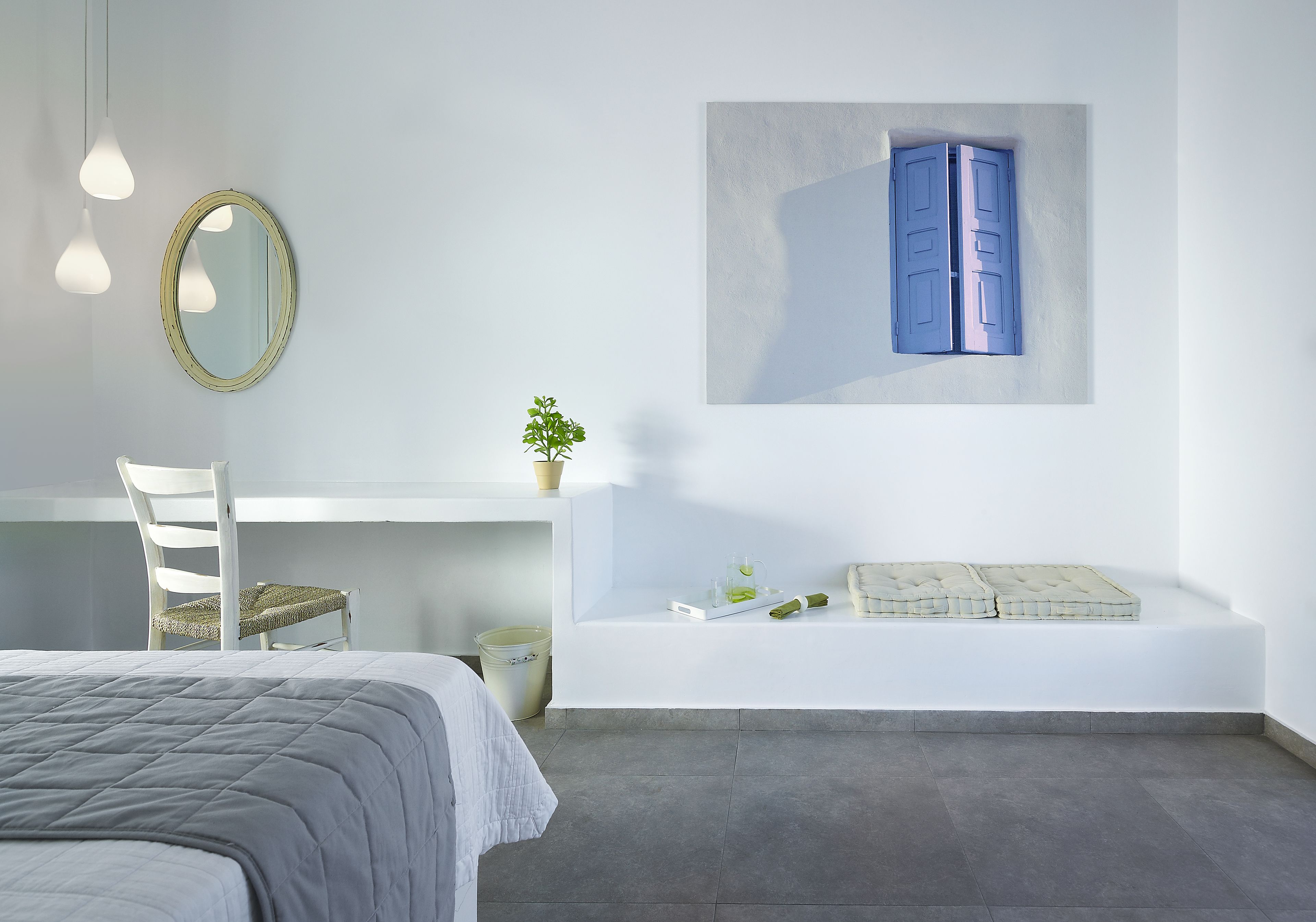 Un dormitorio moderno con cama, escritorio, silla, mesita con planta y estante en la pared con cojín y adornos.