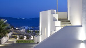 A modern building with a staircase leading to a balcony overlooking a body of water. - Santa Maria Luxury Suites & Spa (Milos)
