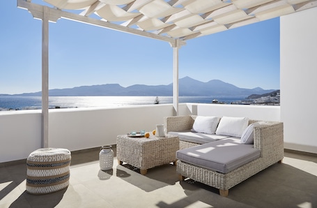 A balcony with wicker furniture, a glass of water, and a view of the sea and mountains.