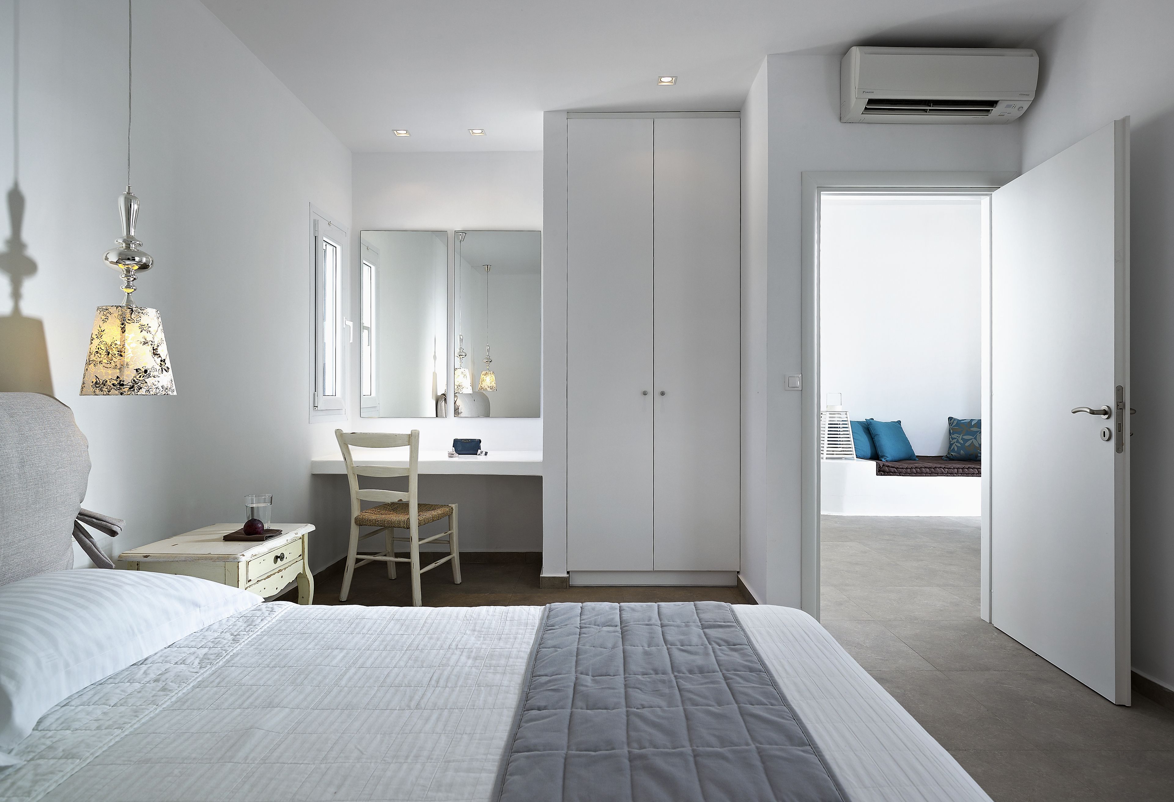 A bedroom with a bed, bedside table, chair, desk, wardrobe, and a view of the balcony.