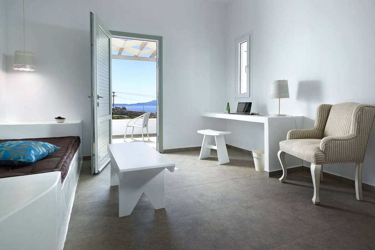 Ein modernes, minimalistisches Zimmer mit Balkon, Schreibtisch, Stuhl und Bett.
