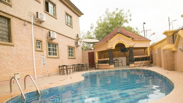 Une piscine dotée d’une terrasse carrelée, d’un espace salon couvert et d’un bâtiment avec de nombreuses fenêtres et des unités de climatisation.