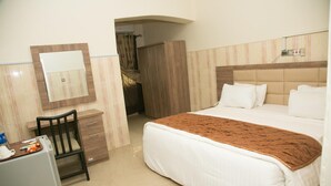 Une chambre d’hôtel comprenant un lit, un bureau, une chaise, une armoire et un miroir.