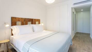 A bedroom with a wooden headboard, white bedding, a bedside table, and a chandelier.