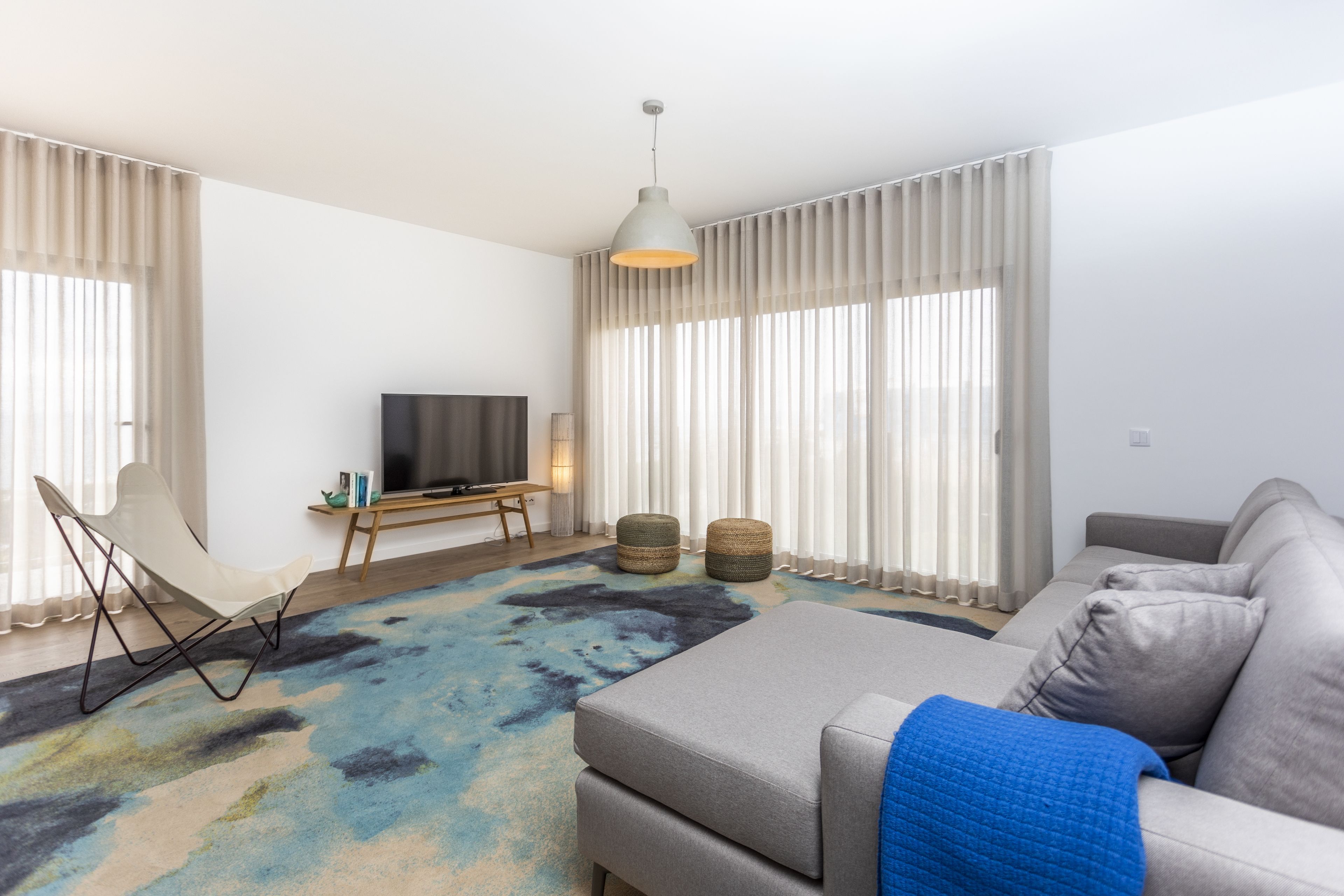 Een moderne woonkamer met een bank, een voetenbankje en een televisie op een houten dressoir.