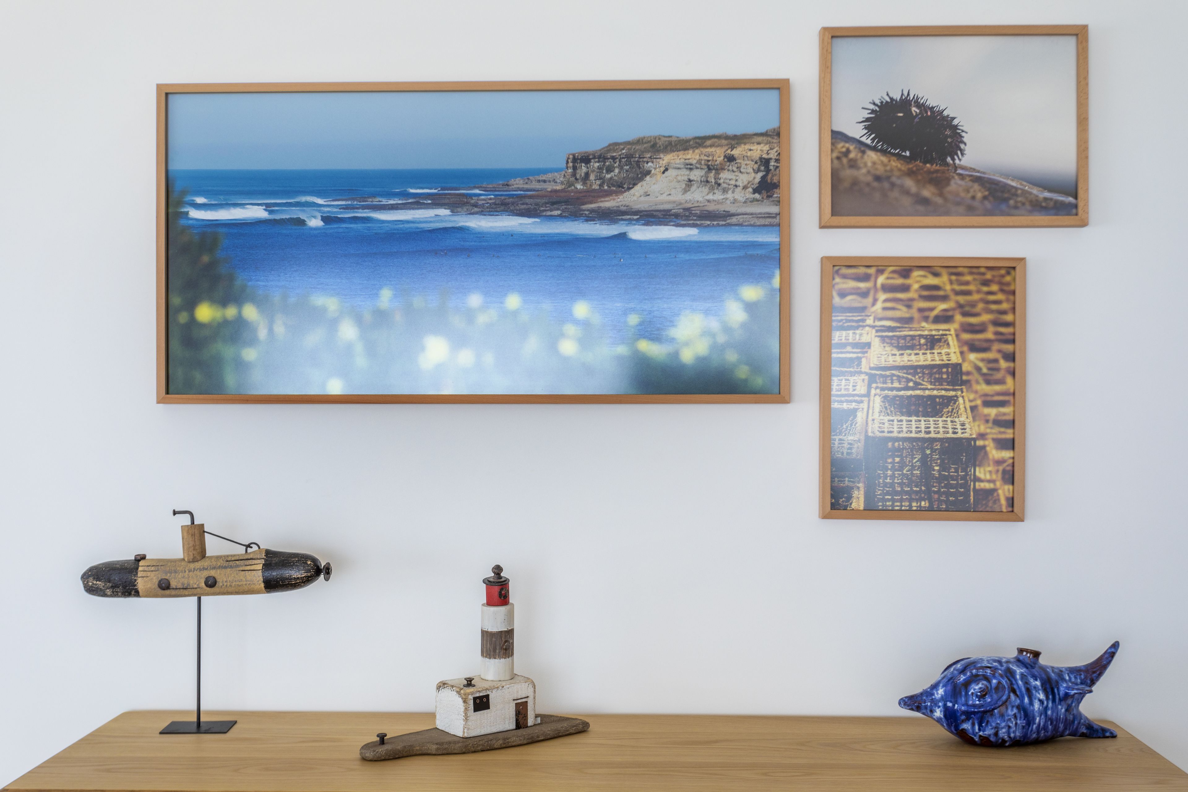 A wall with three framed pictures, a model submarine, a lighthouse, and a fish sculpture.