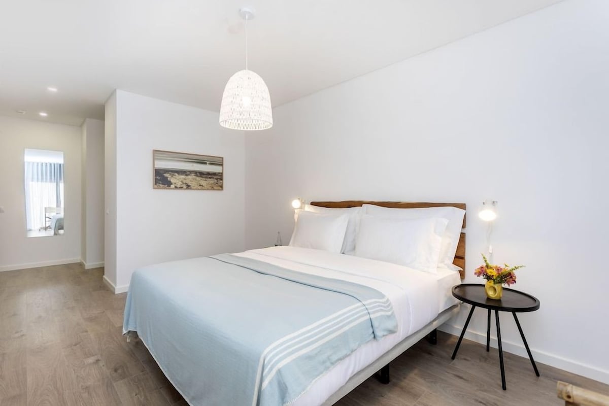 A bedroom with a bed, bedside table, lamp, and a painting on the wall.