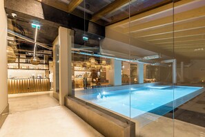 An indoor swimming pool with a glass barrier, a bar area with bottles, and a modern architectural design. - You and the sea (Mafra)