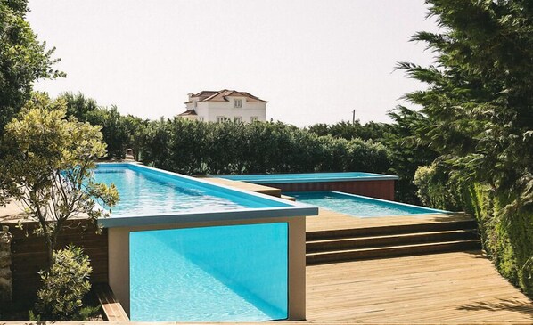 A swimming pool area with two rectangular pools, surrounded by wooden decking and lush greenery. - You and the sea (Mafra)