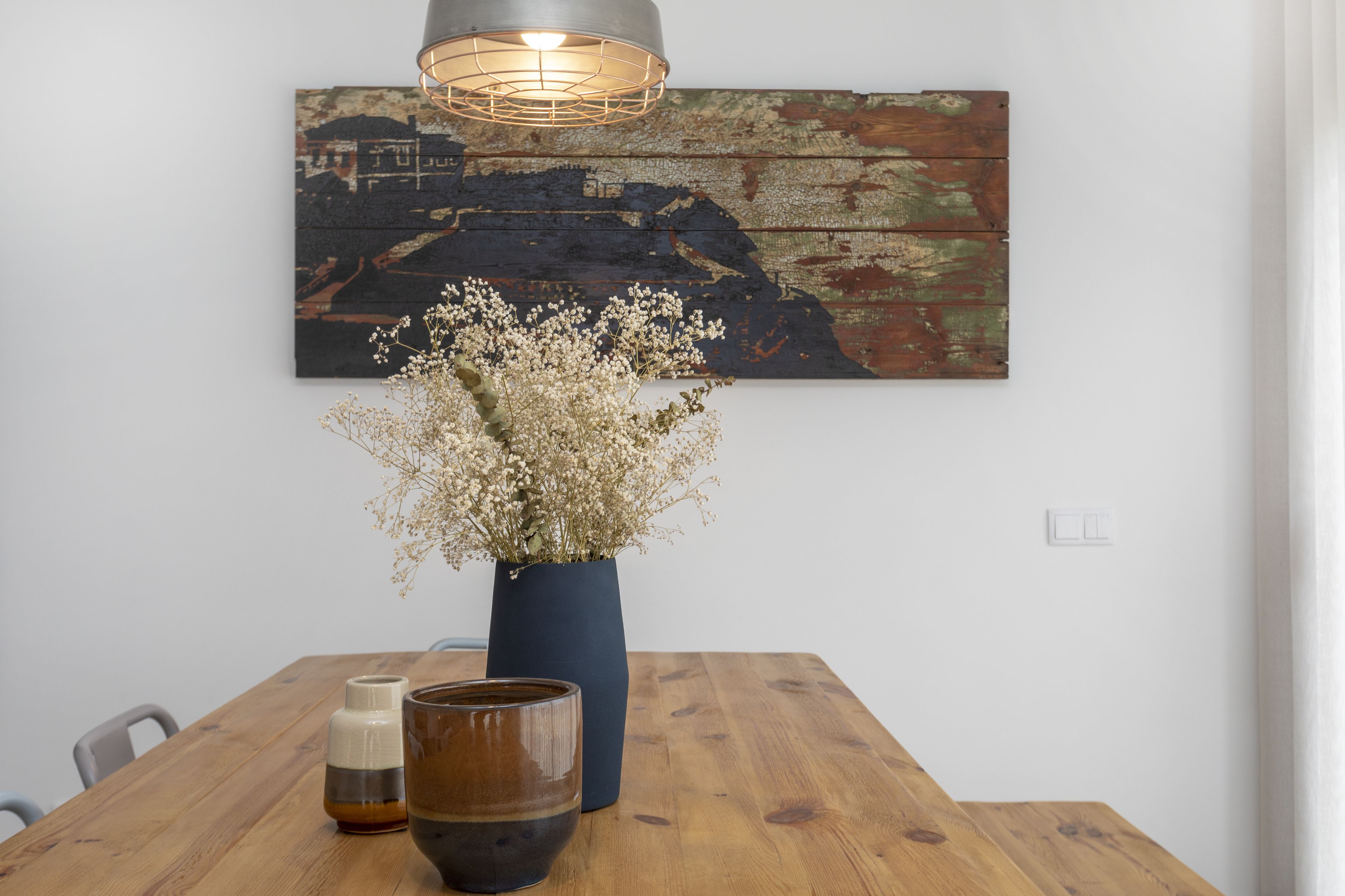 A wooden dining table with a vase of dried flowers, a candle, and a glass.