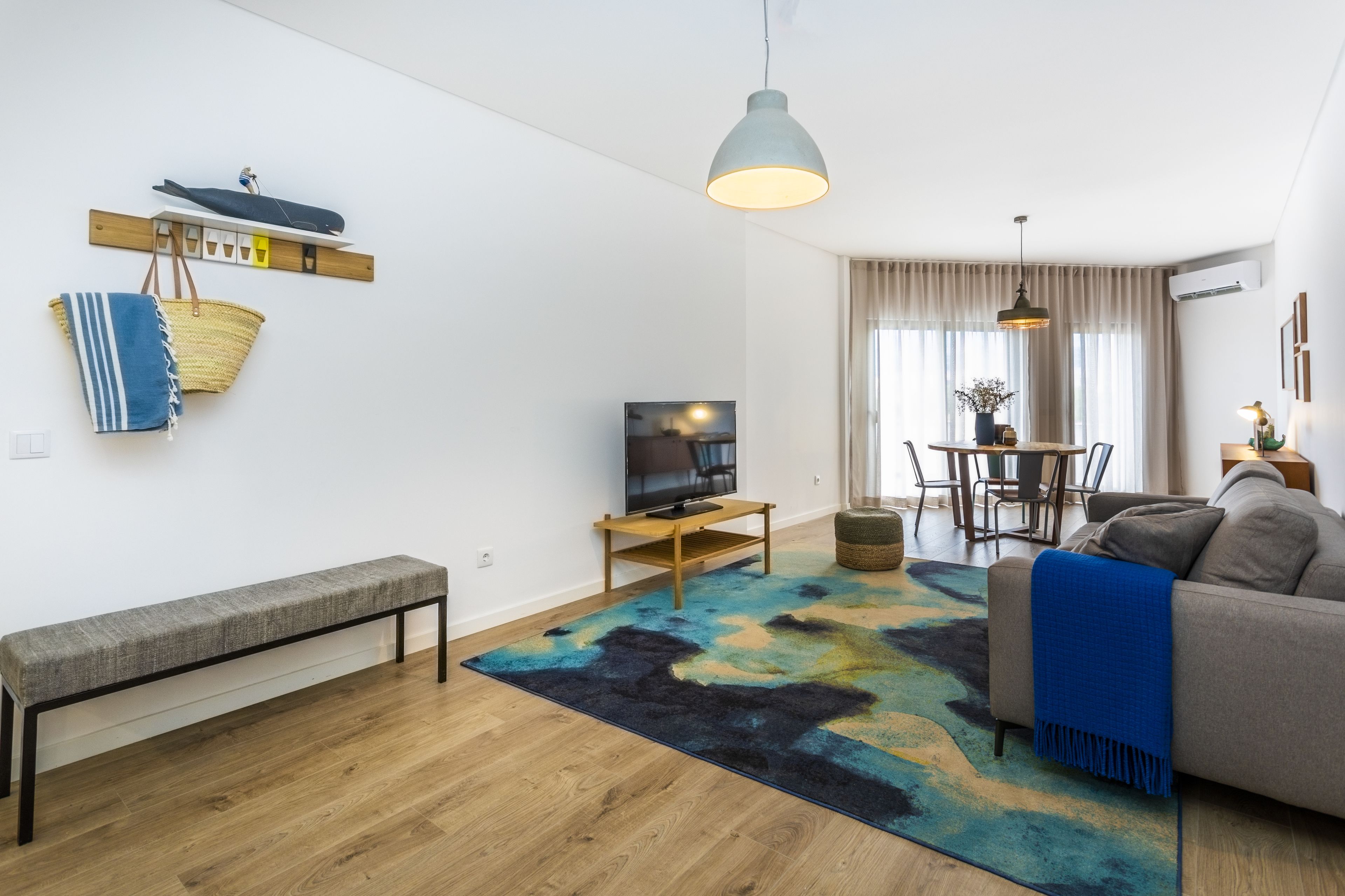 Una sala de estar moderna con un sofá, un banco, un televisor y un comedor con mesa y sillas.