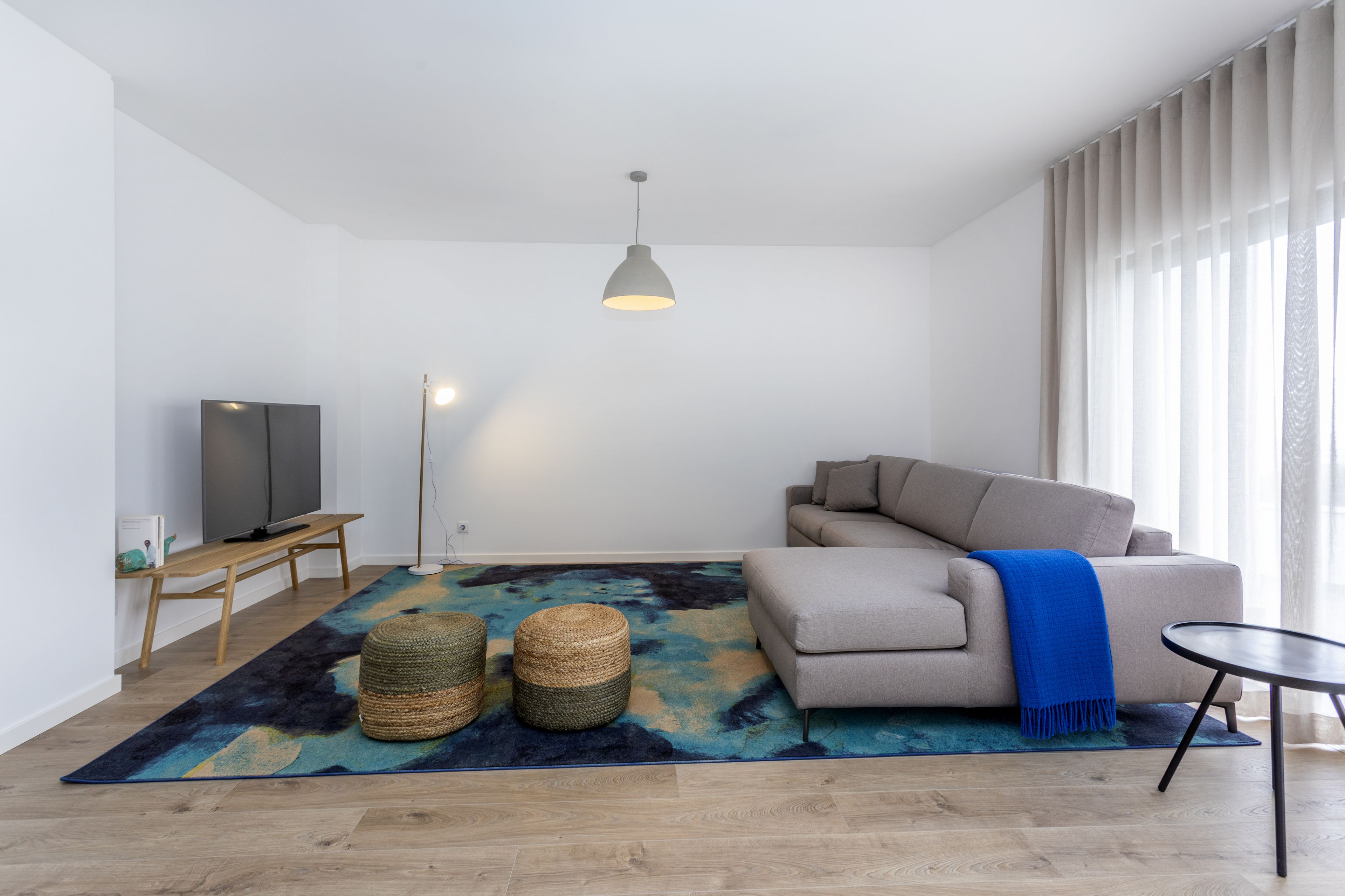 A modern living room with a sofa, a TV, a floor lamp, and a large window with curtains.