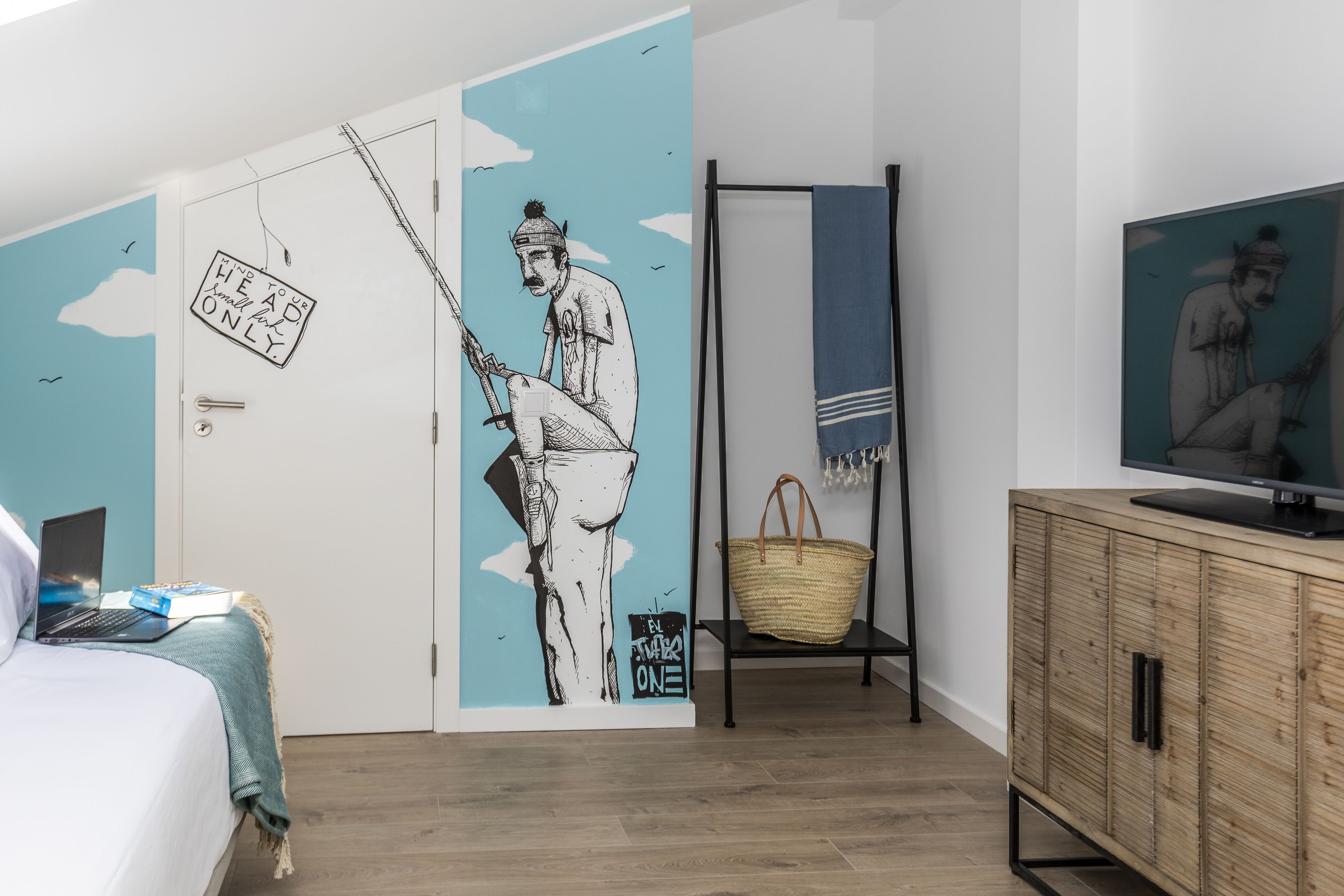 Una camera da letto con un letto, un portatile, una TV e una parete con un murale.
