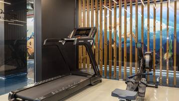 A treadmill and rowing machine in a gym with a mural of a desert landscape.