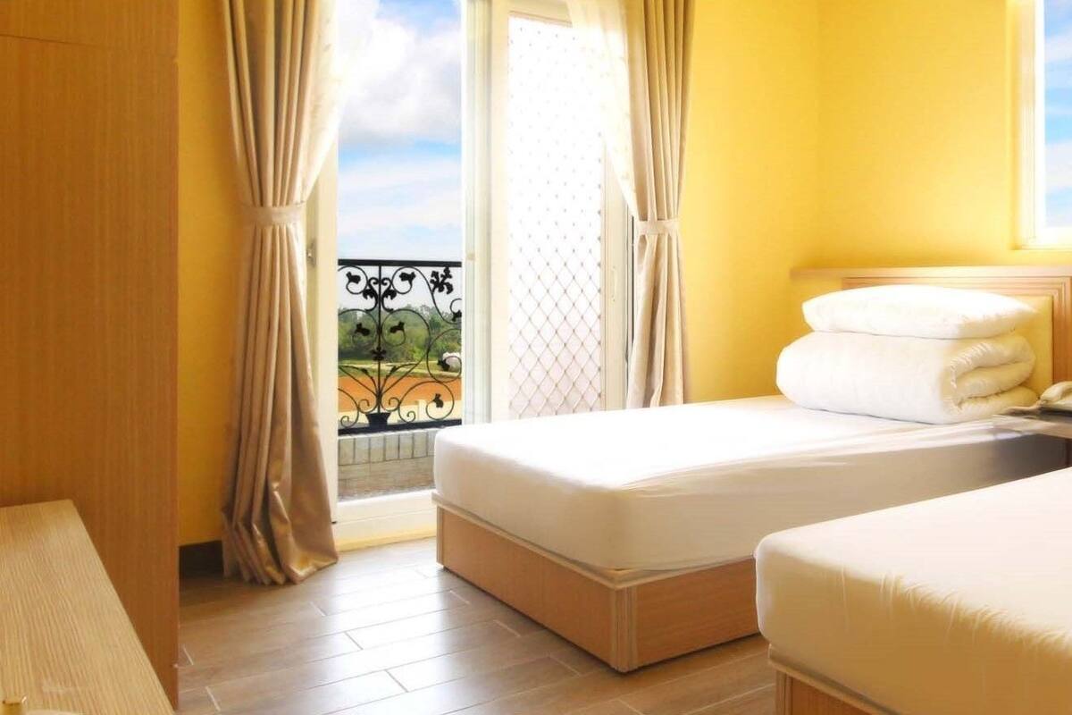 Quarto de hotel com duas camas, varanda e vista para área verde.