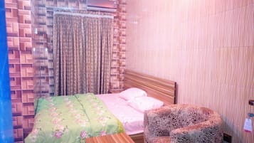 A bedroom with a patterned wall, a bed with floral bedding, and a leopard print chair.