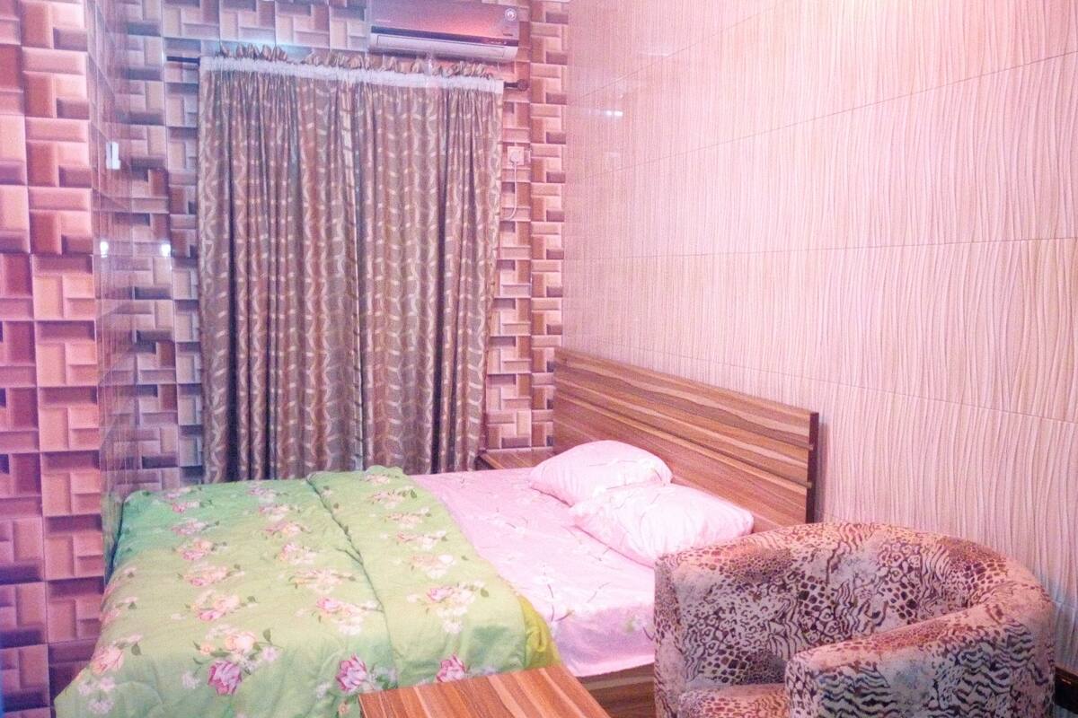Une chambre à coucher avec un lit, une chaise à motifs, un rideau à motifs et un mur orné d’un motif géométrique.