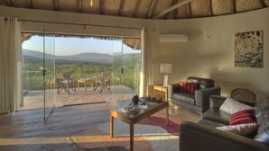 A room with a glass door leading to a balcony with a scenic view. Inside, there is a leather sofa, a wooden coffee table, and a small table with a lamp. - Spirit Of The Masai Mara (Maasai Mara)