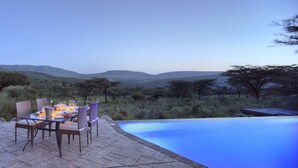 An outdoor dining area with a pool, surrounded by a natural landscape with hills and sparse trees. - Spirit Of The Masai Mara (Maasai Mara)