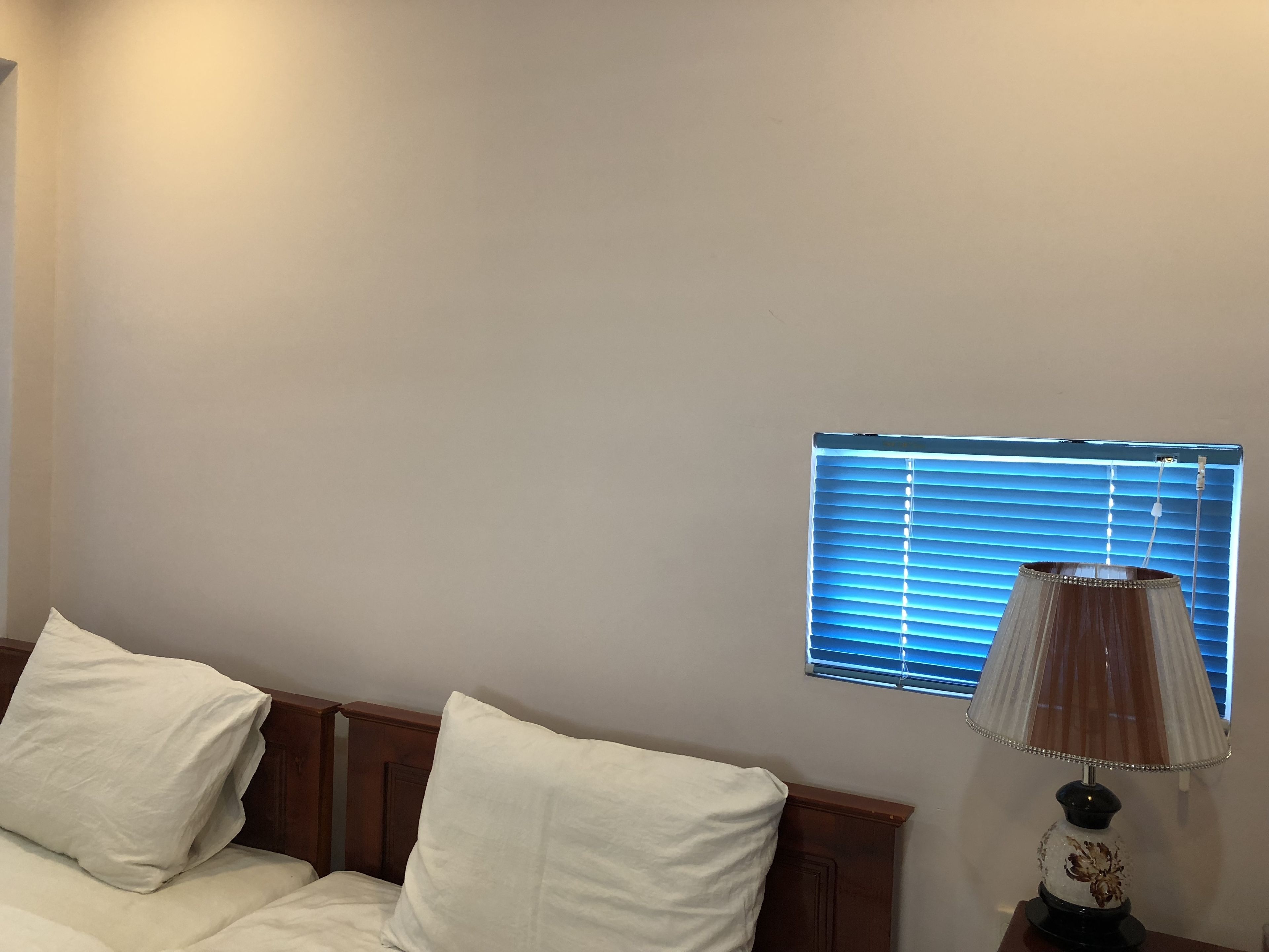 A bedroom with a bed, pillows, a nightstand, a lamp, and a window with blinds.