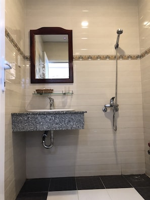 A bathroom with a granite sink, a mirror with a decorative frame, a showerhead, and a tiled floor.