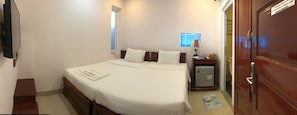 A neatly made bed with white linens, a small bedside table with a lamp, and a refrigerator.