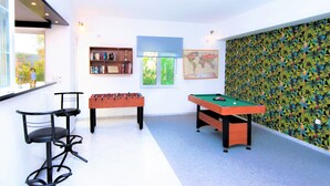 Ein Raum mit Kickertisch, Billardtisch, Barbereich mit Hockern, einer Bücherwand und einer Weltkarte an der Wand.