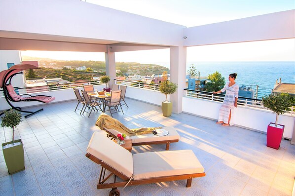 A spacious balcony with lounge chairs, a dining table, and potted plants.