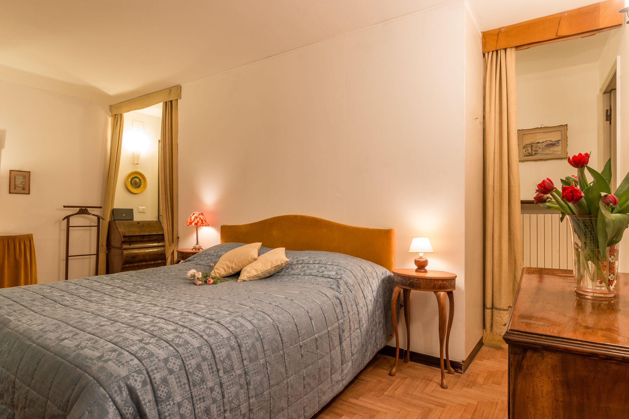 A neatly made bed with a patterned bedspread, a small bedside table with a lamp, and a mirror on the wall.