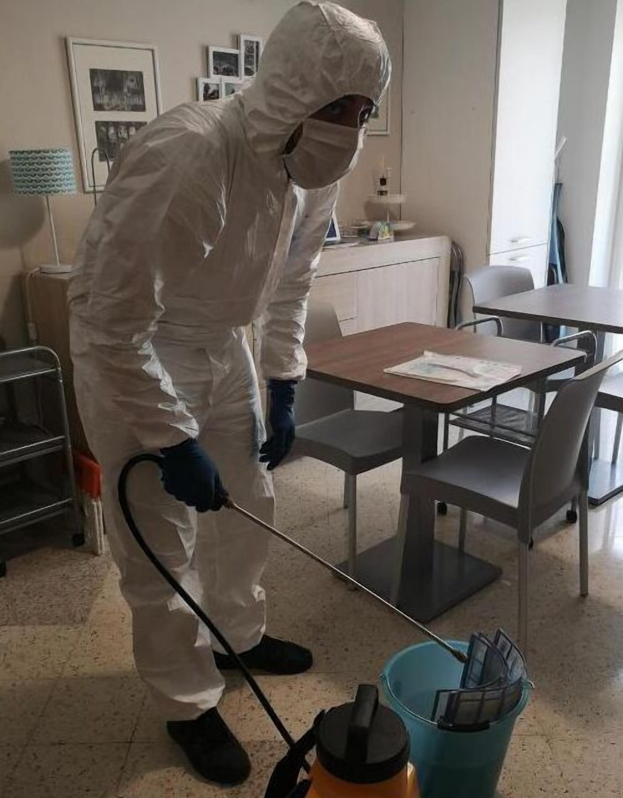 A person in a white protective suit cleaning a room with a vacuum cleaner.