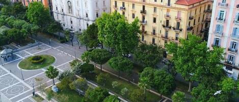 An aerial view of a cityscape with multi-story buildings, a roundabout, and a well-maintained green space with trees.
