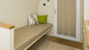 Una habitación pequeña con una cama, una puerta con persianas, un panel de control reducido y una lámpara en el techo.