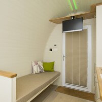Una habitación pequeña con una cama, una puerta con persianas, un panel de control reducido y una lámpara en el techo.