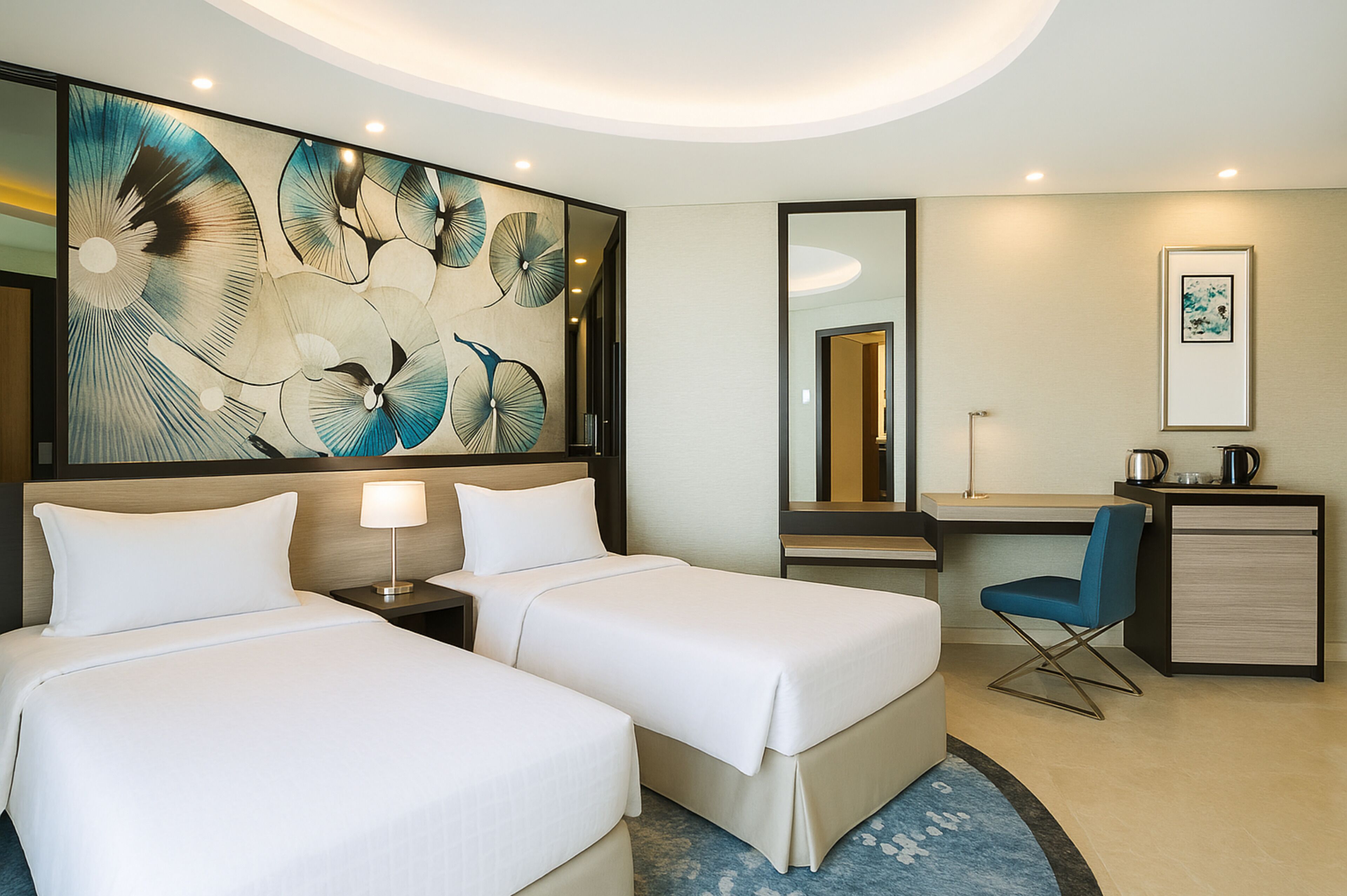 A hotel room with two beds, a desk, a chair, a mirror, and a large abstract painting on the wall.