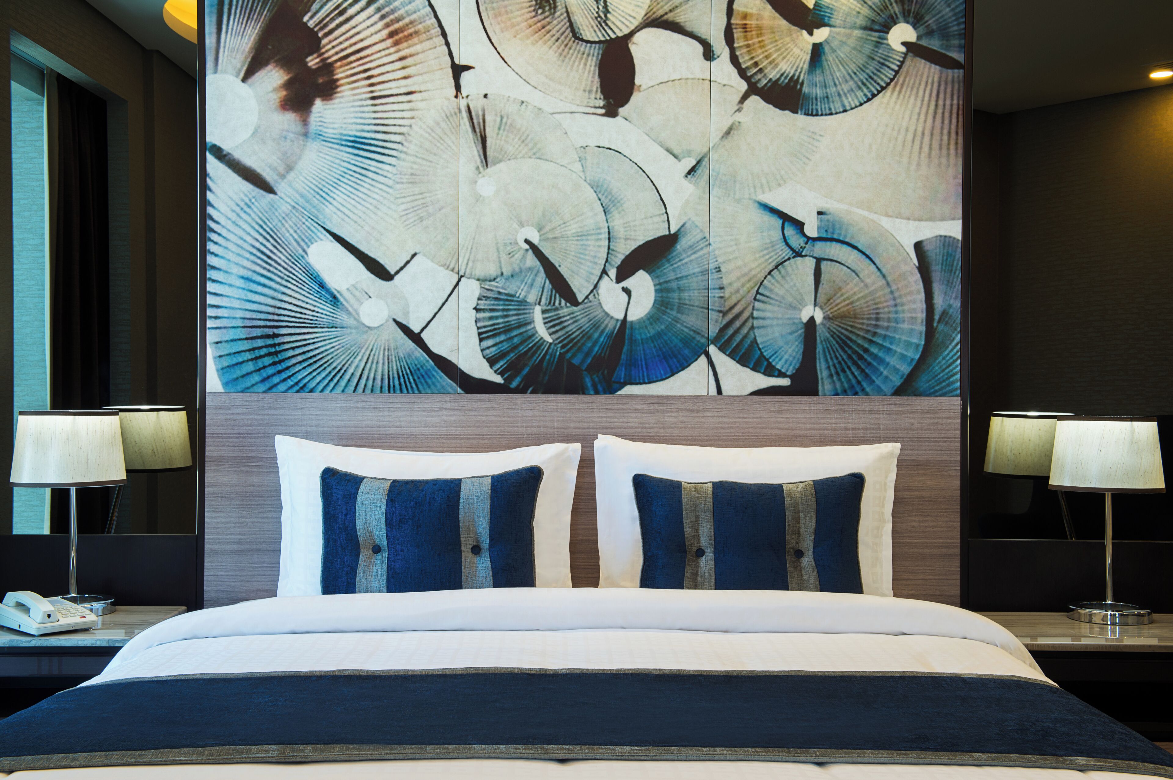 A hotel room with a large bed, two bedside tables with lamps, and a wall with a large abstract painting.