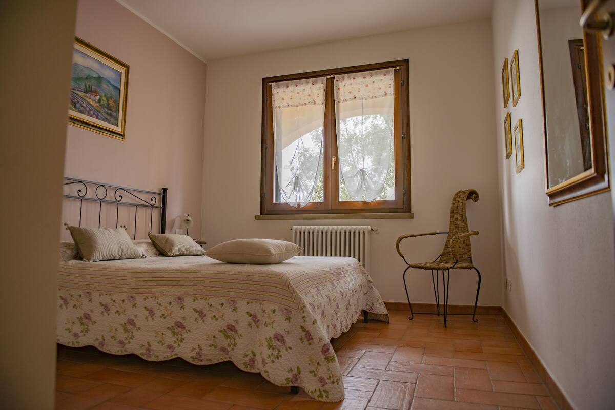 Een slaapkamer met een bed, een stoel, een raam en een radiator.