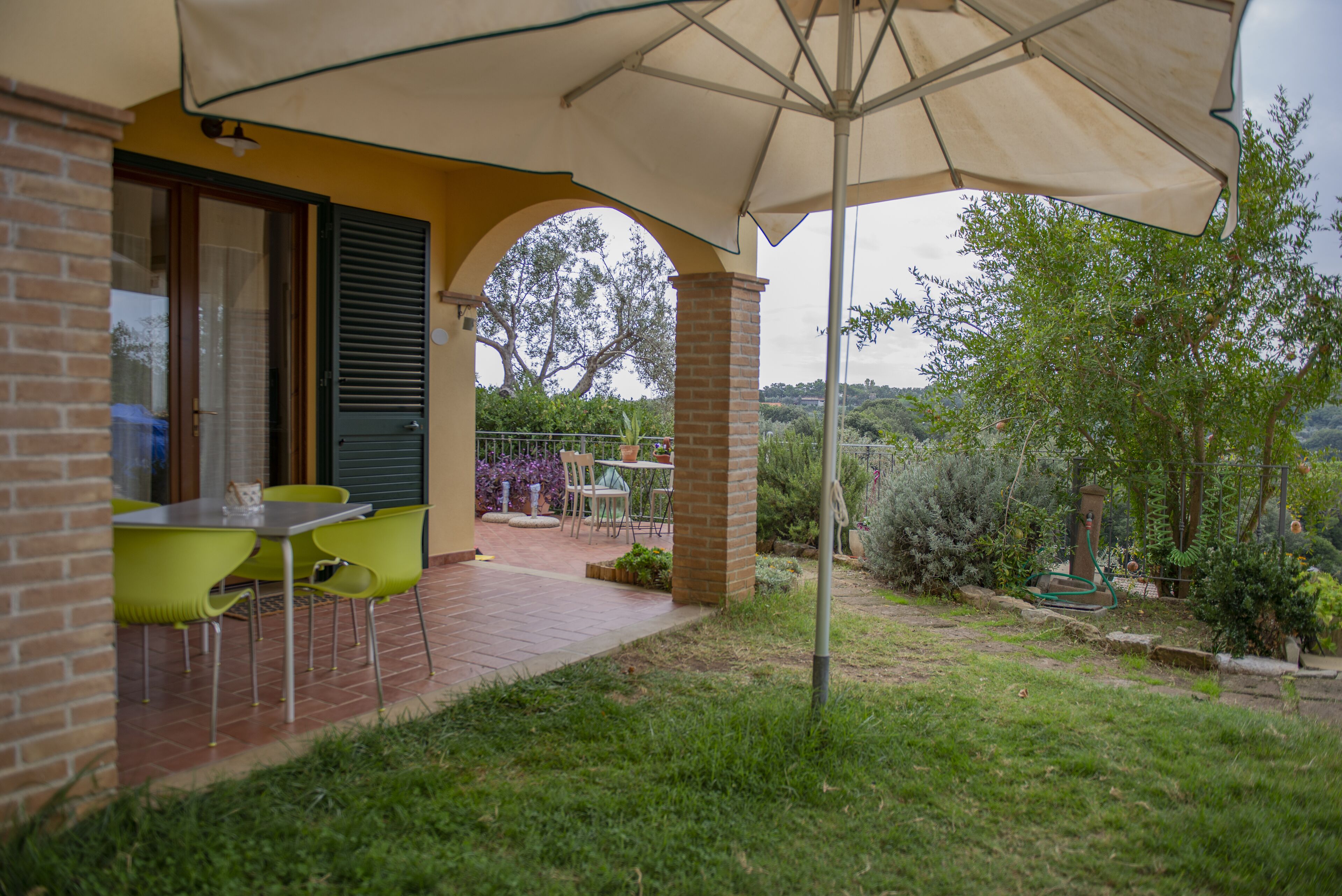 An outdoor patio with a table and chairs, a brick wall, and a view of the surrounding garden and hills.