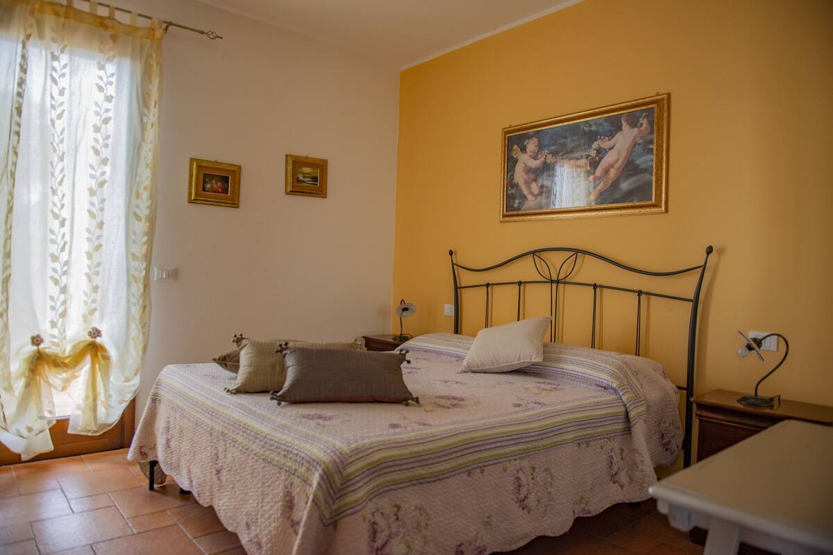 Een slaapkamer met een bed, nachtkastje, lamp en een schilderij aan de muur.