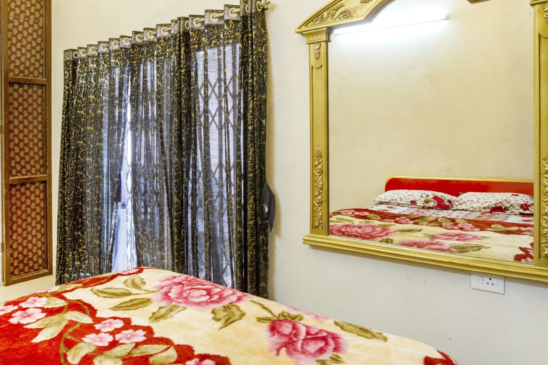 A bedroom with a bed, floral bedspread, a mirror, and curtains.