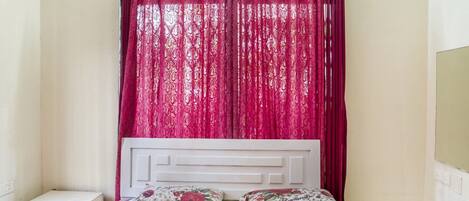 A bedroom with a bed, two pillows, a nightstand, and a window with red curtains.