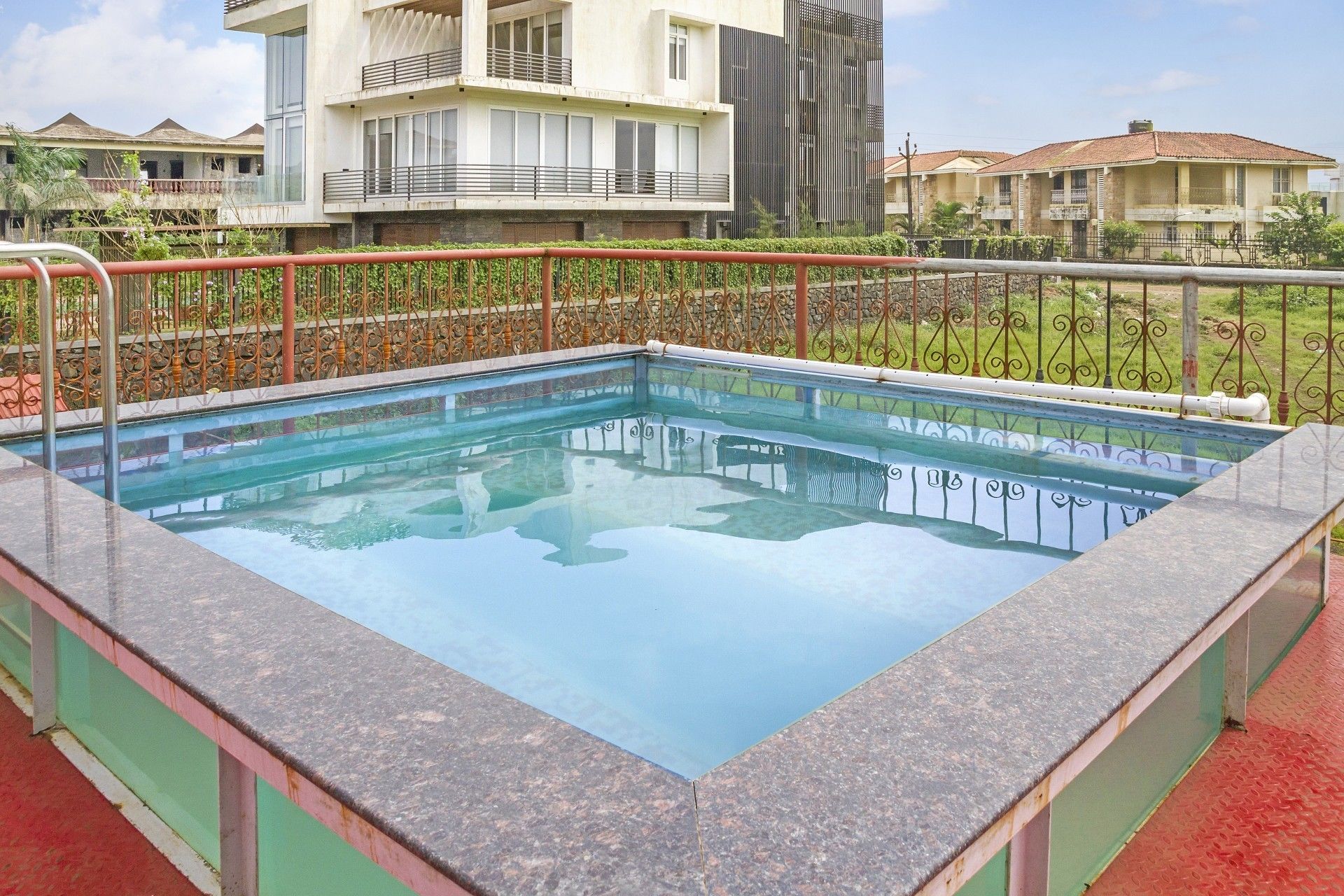 A rectangular pool with a metal railing, surrounded by a low wall and a paved area.