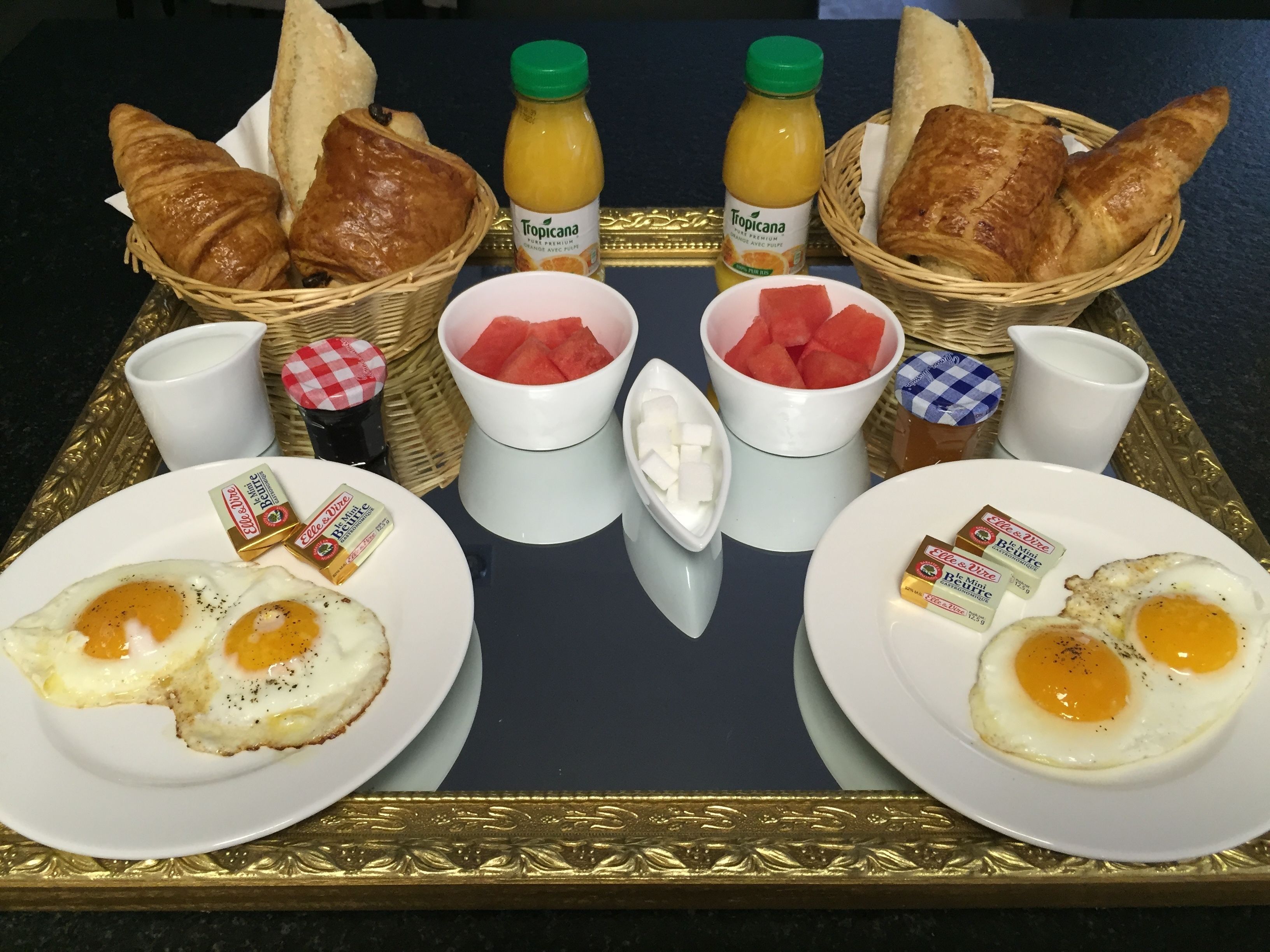 Een ontbijfwagen met croissants, watermeloen, sap en twee borden met eieren.