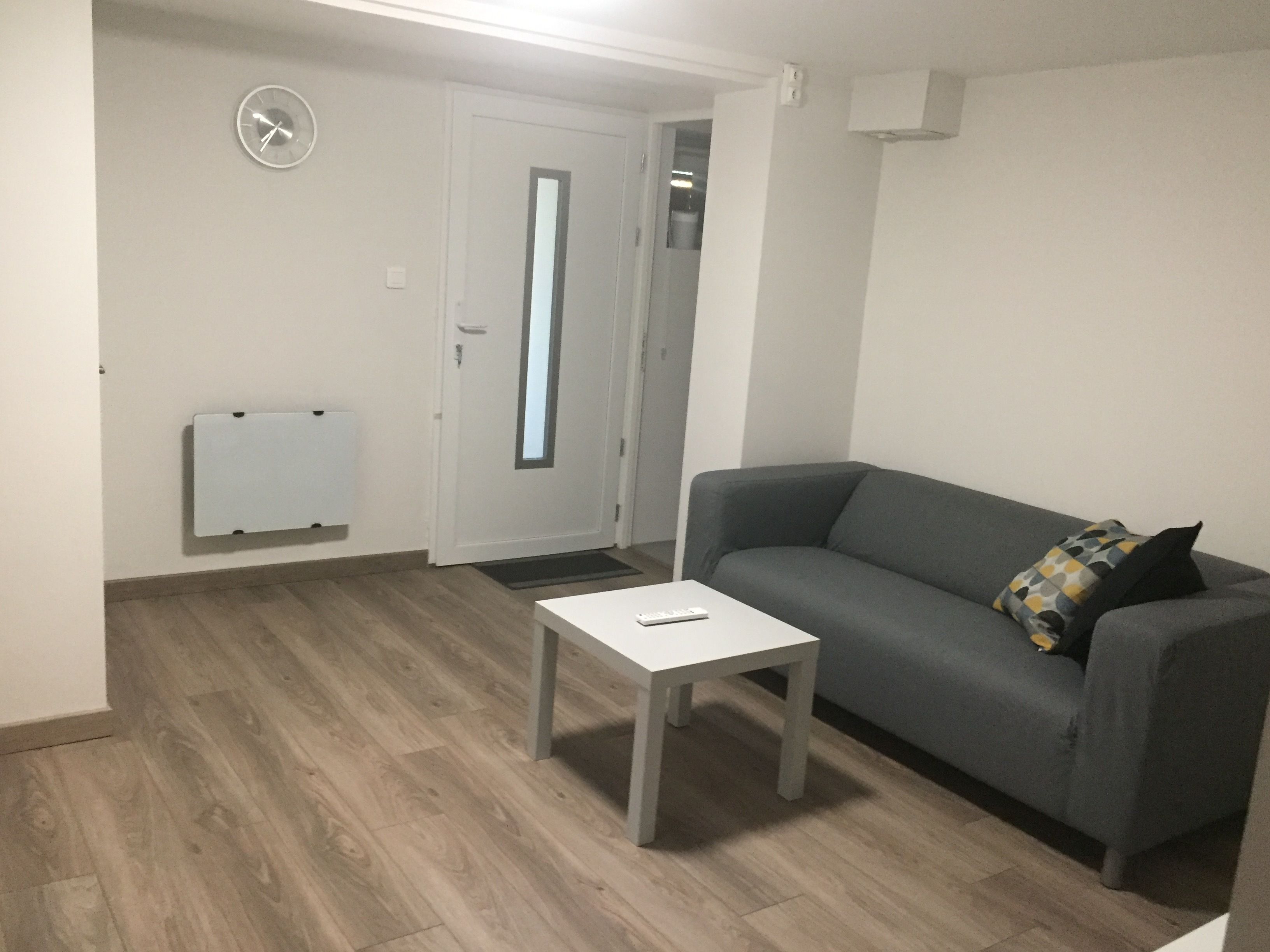 Un salon avec un canapé gris, une table basse blanche et une horloge au mur.