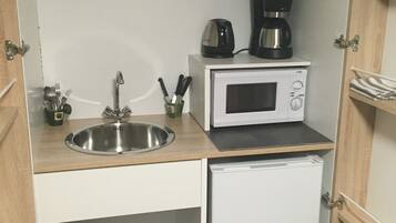 A compact kitchen with a sink, a microwave, a coffee maker, and a small refrigerator.