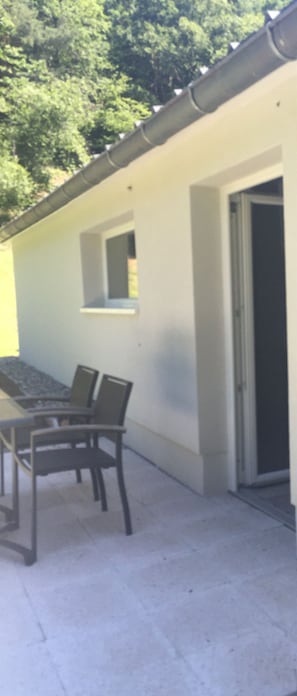 Ein Patio im Freien mit Tisch und Stühlen, einem kleinen Fenster und einer Tür zu einem überdachten Eingang.
