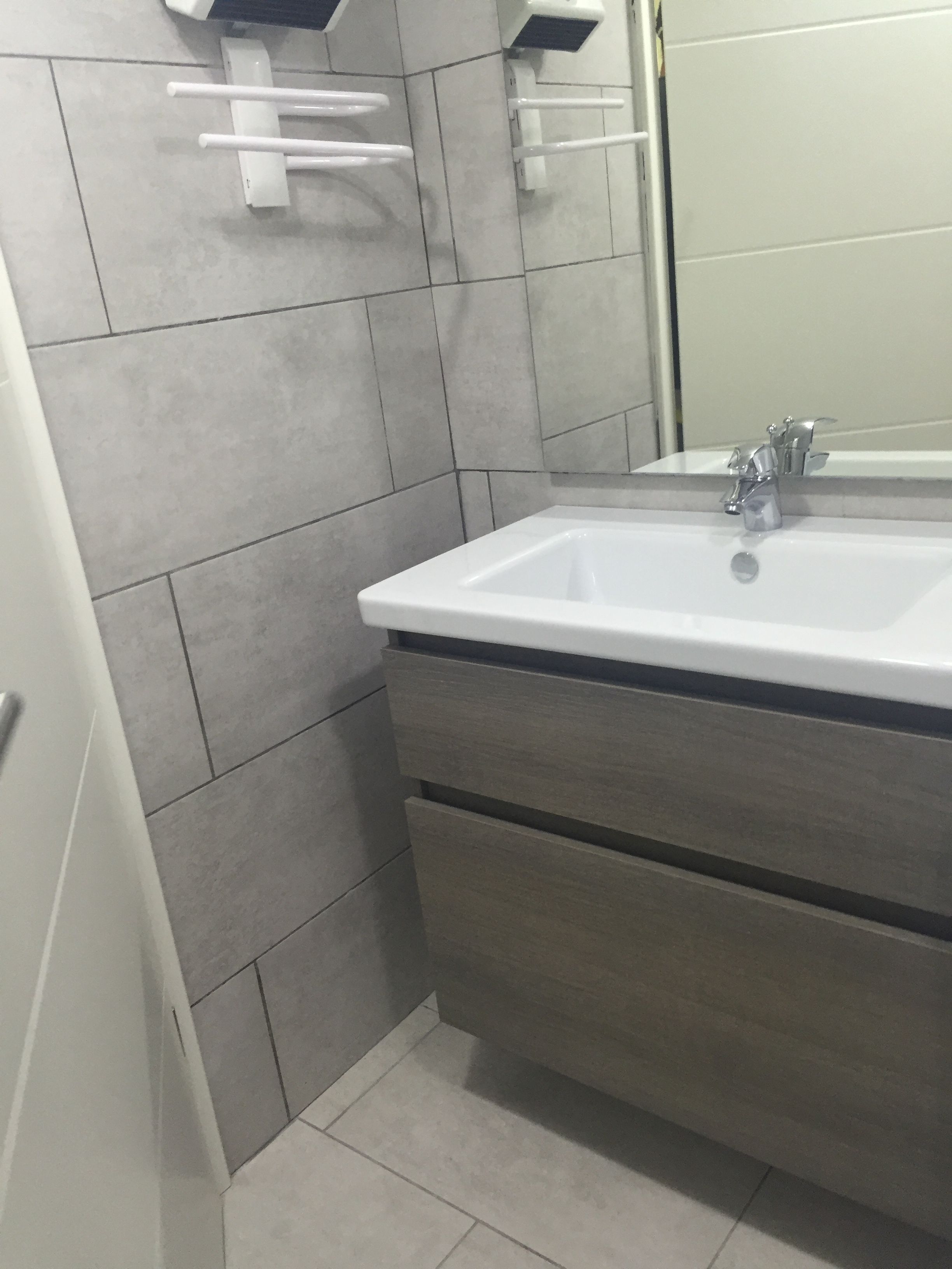 Ein Badezimmer mit weißem Waschbecken, einem Spiegel und grauen Fliesenwänden.