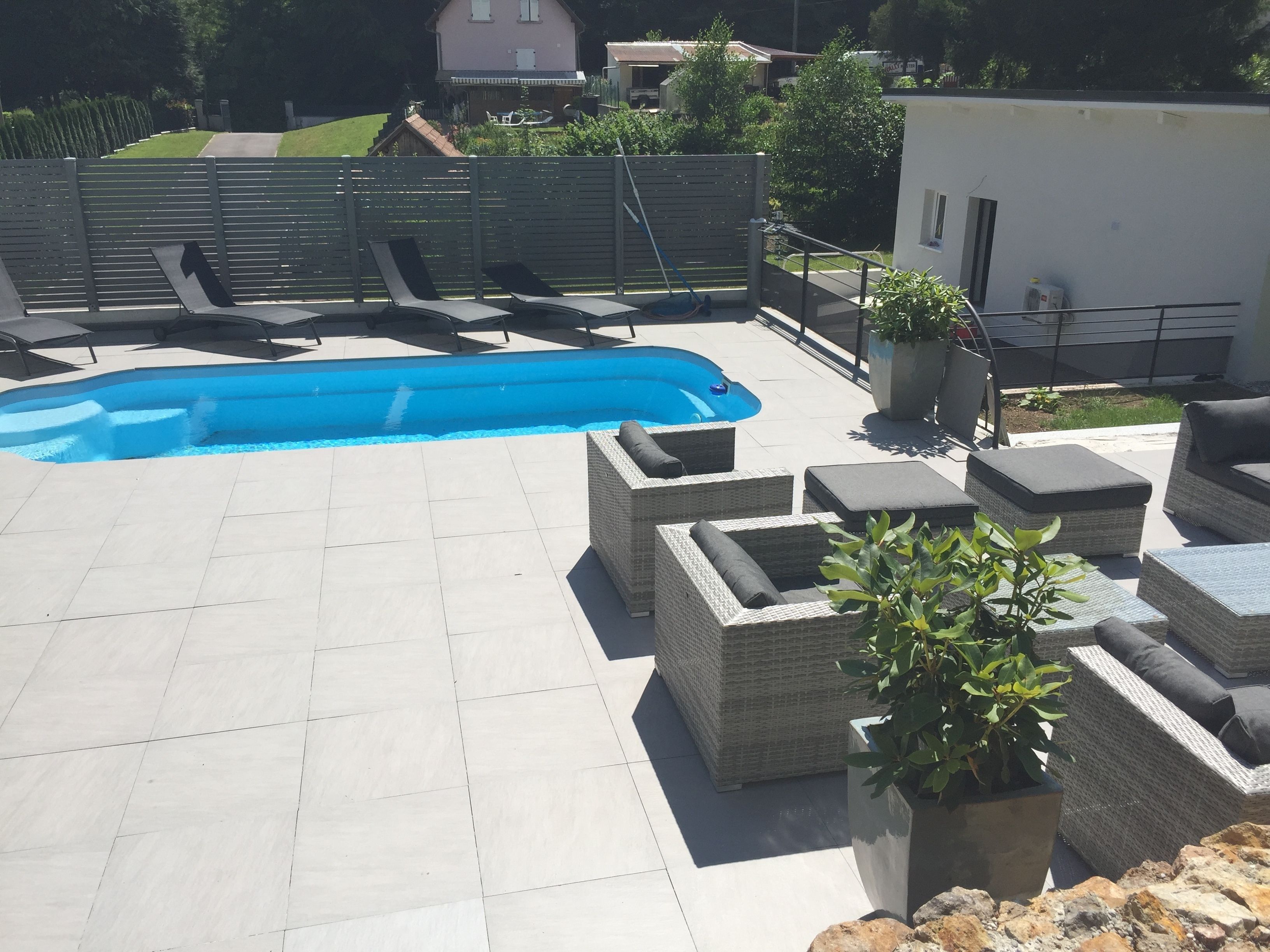 Un área de piscina en la azotea con piscina azul, mobiliario de mimbre y plantas en macetas.
