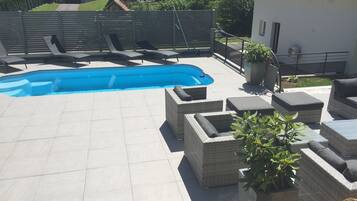 Un área de piscina en la azotea con piscina azul, mobiliario de mimbre y plantas en macetas.